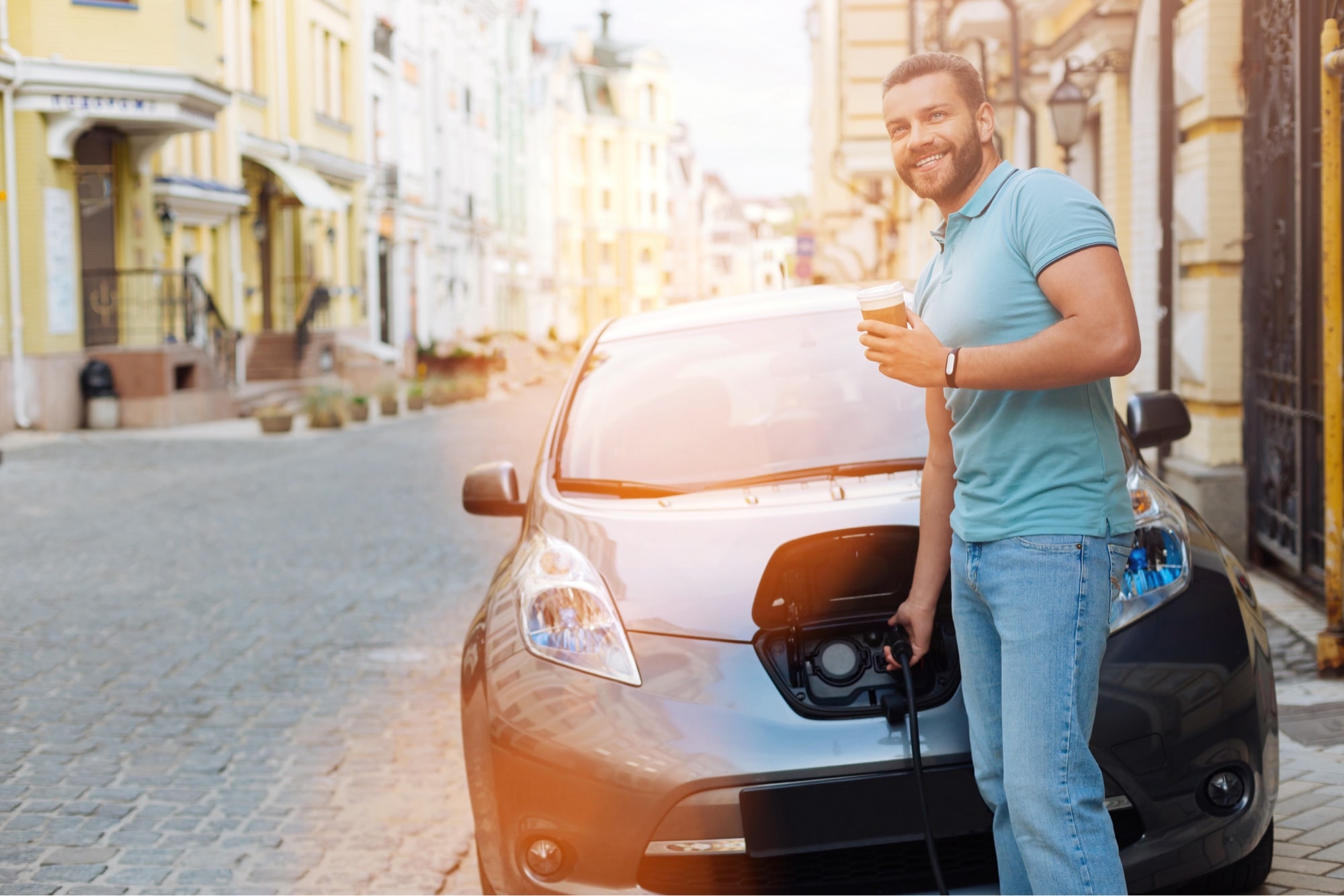 man with coffee charging electric car